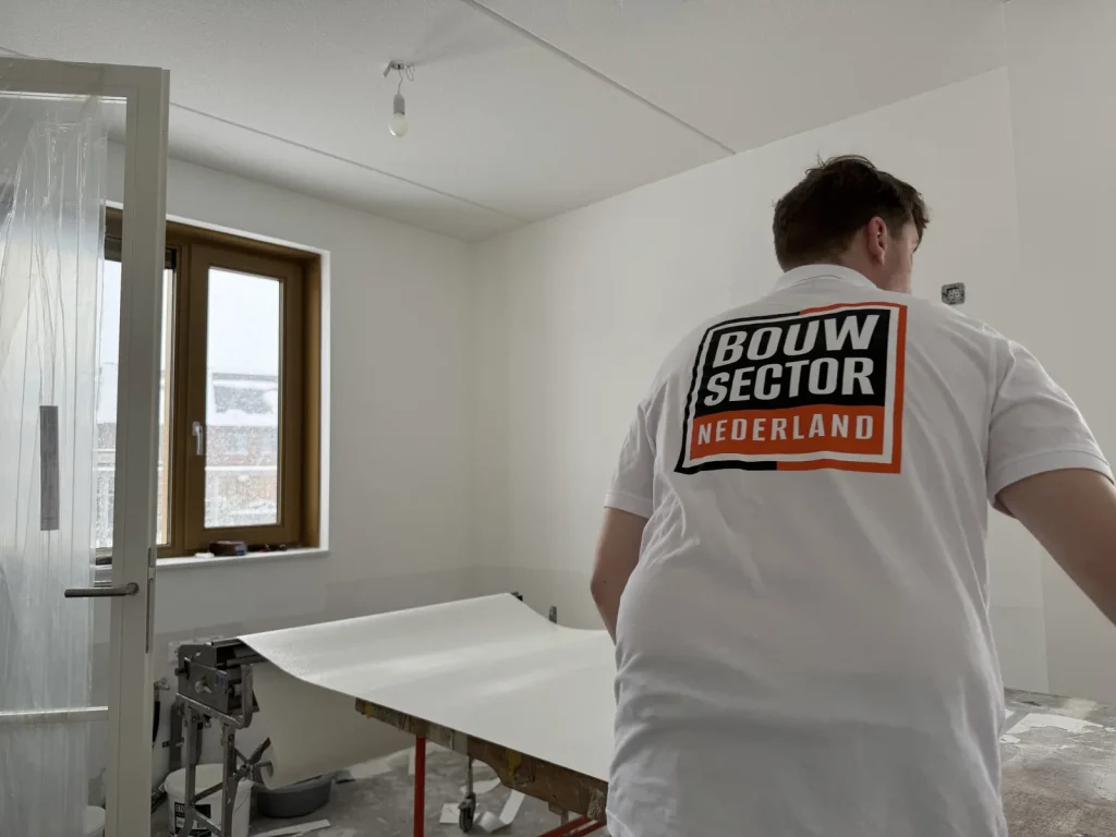 Vakman in Bouwsector-shirt trekt een baan renovlies over de plaktafel in een lege kamer