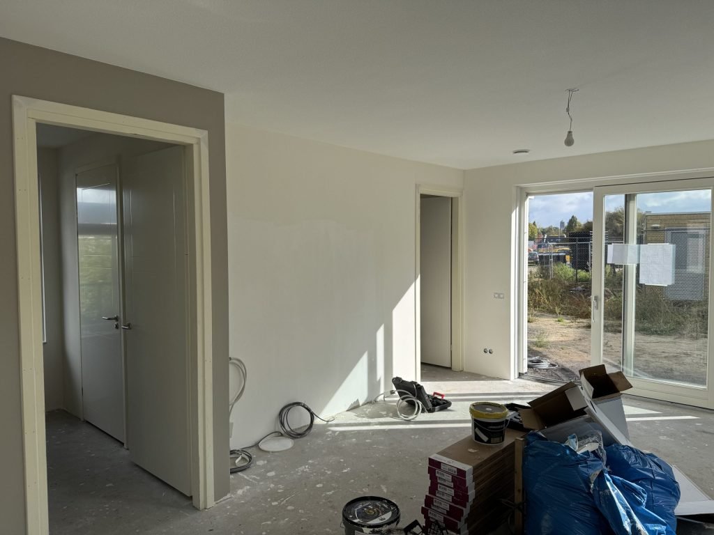 Opgeleverde nieuwbouwwoning met kale betonvloer, dozen laminaat en afgewerkte lichte wanden