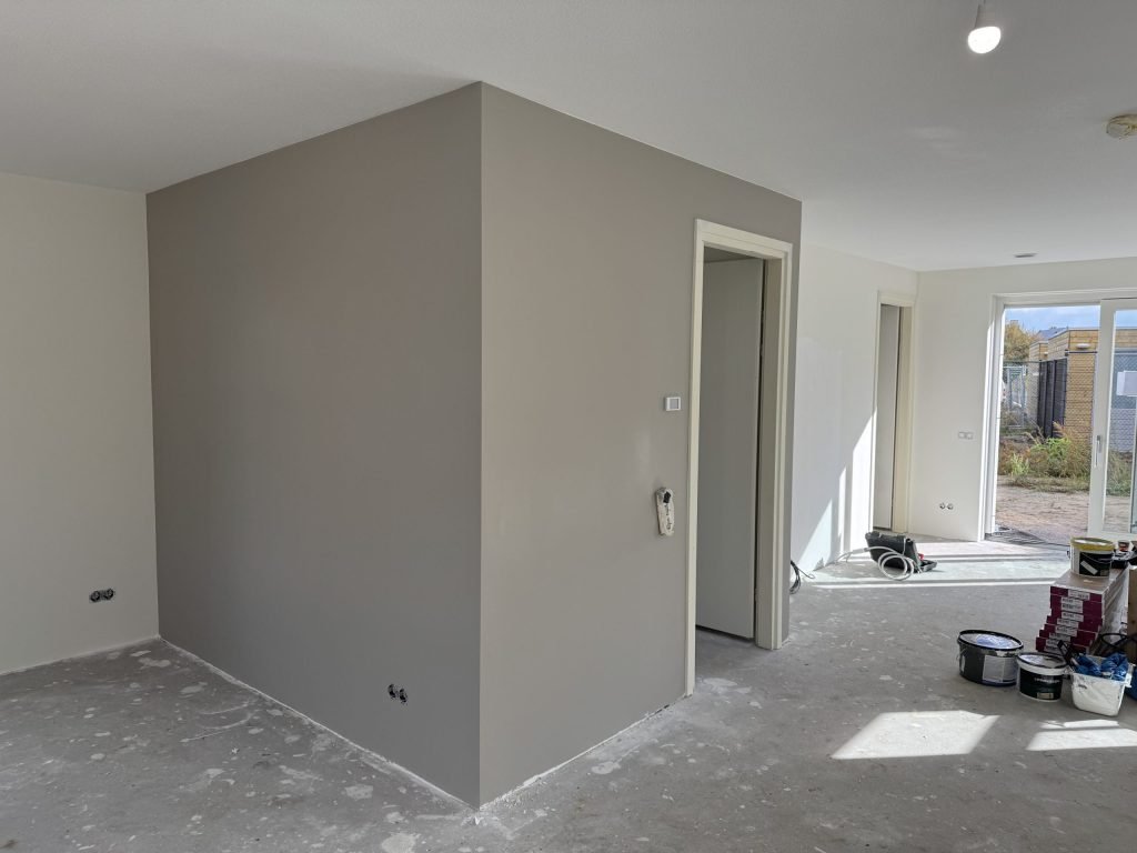 Nieuwbouwwoonkamer met een taupe geverfde muur rond de meterkast en witte wanden eromheen