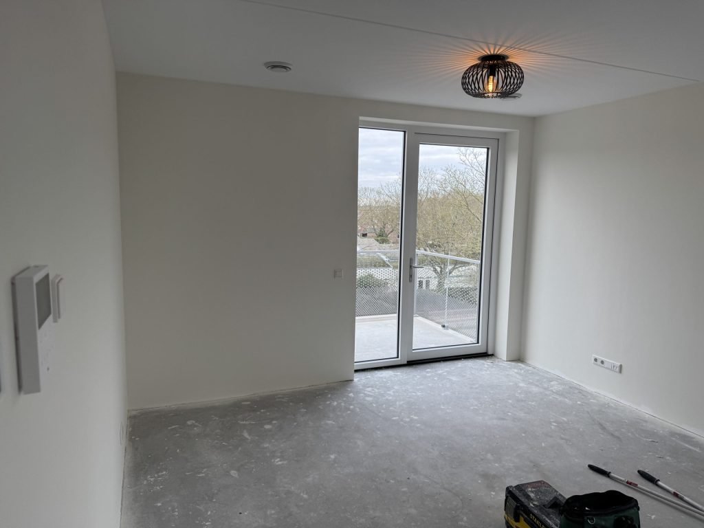Lege kamer met strakke witte wanden en een balkondeur, klaar na het behangen en sauzen